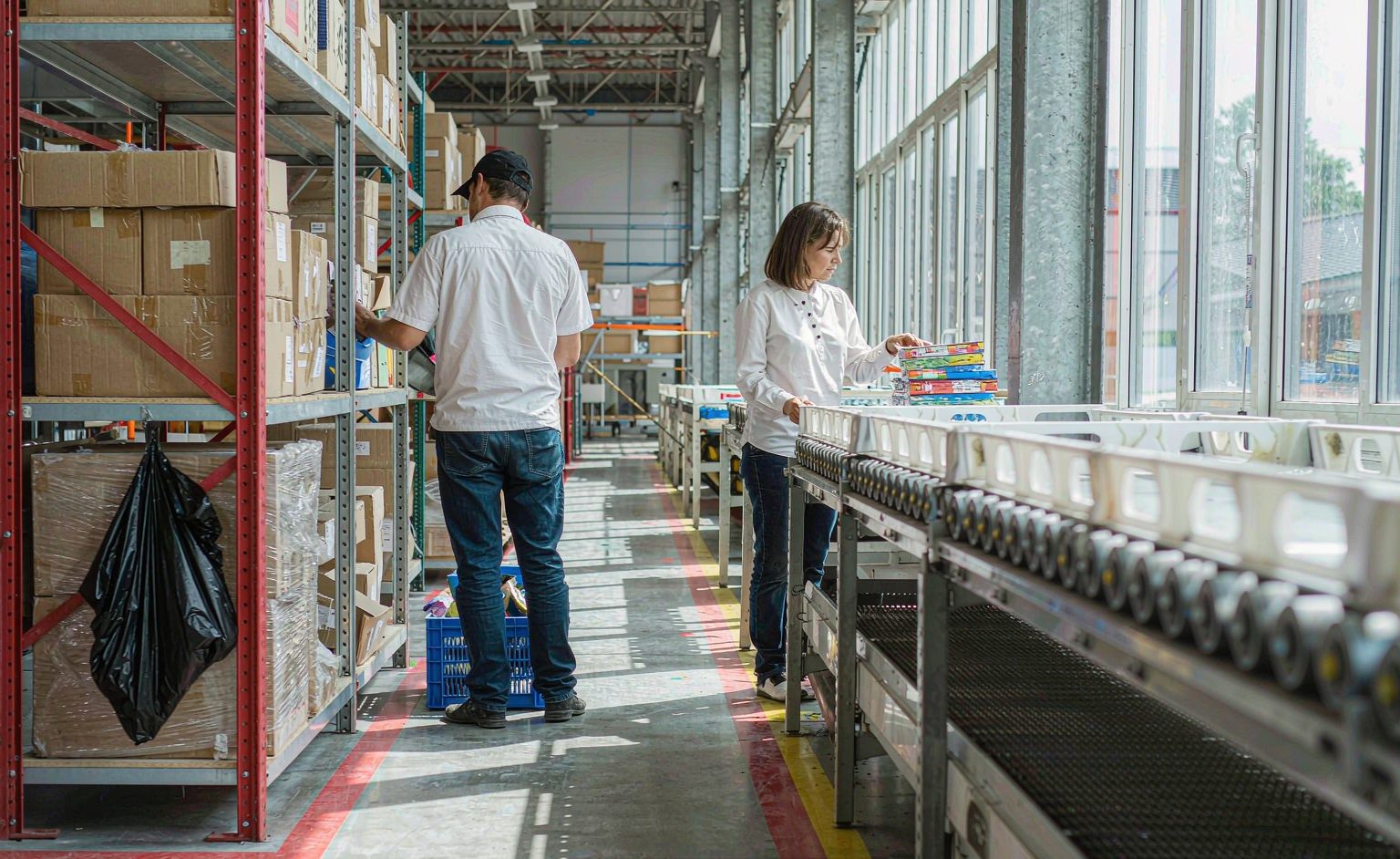 Warehouse Picking Zone Layout Workers picking parcels from shelving beside a conveyor line with marked floor zones